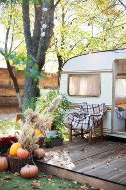 Yeşil bitkilerle çevrili iç taraftaki bir kamp alanı. Eski karavan römorkunun yanında ekoseli tahta koltuk. Bahçe mobilyalarıyla ahşap karavan evi verandası. Dekor yaz bahçesi. Bahçede kamp yeri