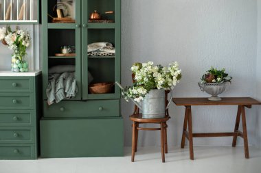 Mobilyalarla dolu bir mutfak. Güzel bir buket çiçek, ahşap koltukta, dolapta. Bahçe işleri konsepti. Klasik bahçe aracı. Vazoda çiçekli şık bir mutfak. Konforlu ev dekorasyonu