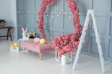 Pembe kanepede bahar evi, duvarda çiçek açan büyük sakura çelengi. Modern iç dekorasyon evi. Paskalya tarzı çocuk odası. Tavşanlı Paskalya dekorasyonu ve yumurtalı kutu.. 