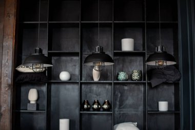 Arka planda eski tarz metal avizeler dekorlu ahşap raflar. Masanın üzerinde üç modern lamba olan karanlık oda. Üç modern siyah tavan lambası odada asılı, yakın plan. Dairenin içi.. 