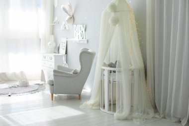 Yeni doğan bebek odasının şık İskandinav iç mimarisi. Yatağı ve gri koltuğu var. Beşikli beyaz bir gölgelik. Mobilyalı çocuk odası dekorasyonu. Modern bir çocuk odasında beşik. Kubbeli bebek karyolası