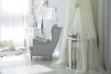 Yeni doğan bebek odasının şık İskandinav iç mimarisi. Yatağı ve gri koltuğu var. Beşikli beyaz bir gölgelik. Mobilyalı çocuk odası dekorasyonu. Modern bir çocuk odasında beşik. Kubbeli bebek karyolası