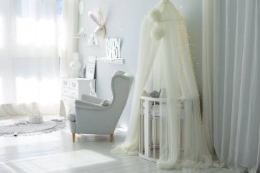 Yeni doğan bebek odasının şık İskandinav iç mimarisi. Yatağı ve gri koltuğu var. Beşikli beyaz bir gölgelik. Mobilyalı çocuk odası dekorasyonu. Modern bir çocuk odasında beşik. Kubbeli bebek karyolası