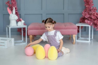 Güzel küçük kız renkli Paskalya yumurtaları ve Paskalya tavşanı ile oynuyor. Aile tatilleri, gelenekler. Küçük çiftçi. Paskalya yumurtası avla. Çocuk Paskalya yumurtalarının peşinde. Devekuşu yumurtası tutan kız.