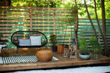 Cozy space in patio or balcony. Wooden verande with garden furniture. Modern lounge outdoors in backyard. Terrace house with plants, wooden wall and table, comfortable sofa, armchair and lanterns.  clipart
