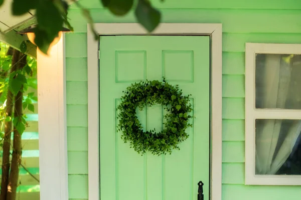CloseUp of green door and decorative wreath. Autumn welcome wreath, decorating front door home. House door with decor with leaves wreath. Autumn cozy decor home for thanksgiving. Summer Decor door