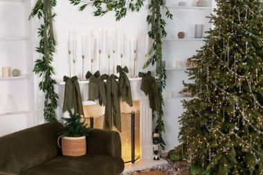 Modern iç mimari oturma odası yeşil kanepeli, süslü Noel ağacı süslemeli ışıklar ve hediyeler, yerde konfeti. Şenlikli Xmas beyaz şömine yaylarla süslenmiş mumlar. Yeni Yıl