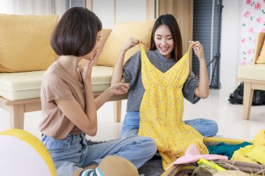 İki genç Asyalı kadın yaz tatili planlıyorlar ve yatak odalarında kıyafet hazırlıyorlar. Yaz ve tatilde seyahat kavramı.