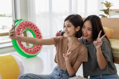 İki genç Asyalı kadın, yaz ve tatil boyunca yatak odalarında bir yaz gezisi planlarken akıllı telefonlarıyla selfie çekiyorlar..