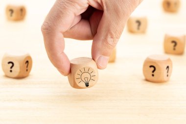 Yaratıcı fikir ya da yenilik kavramı. Tahta masa üzerinde soru işareti sembolü ve ampul simgesi olan elle seçilen tahta küp bloğu