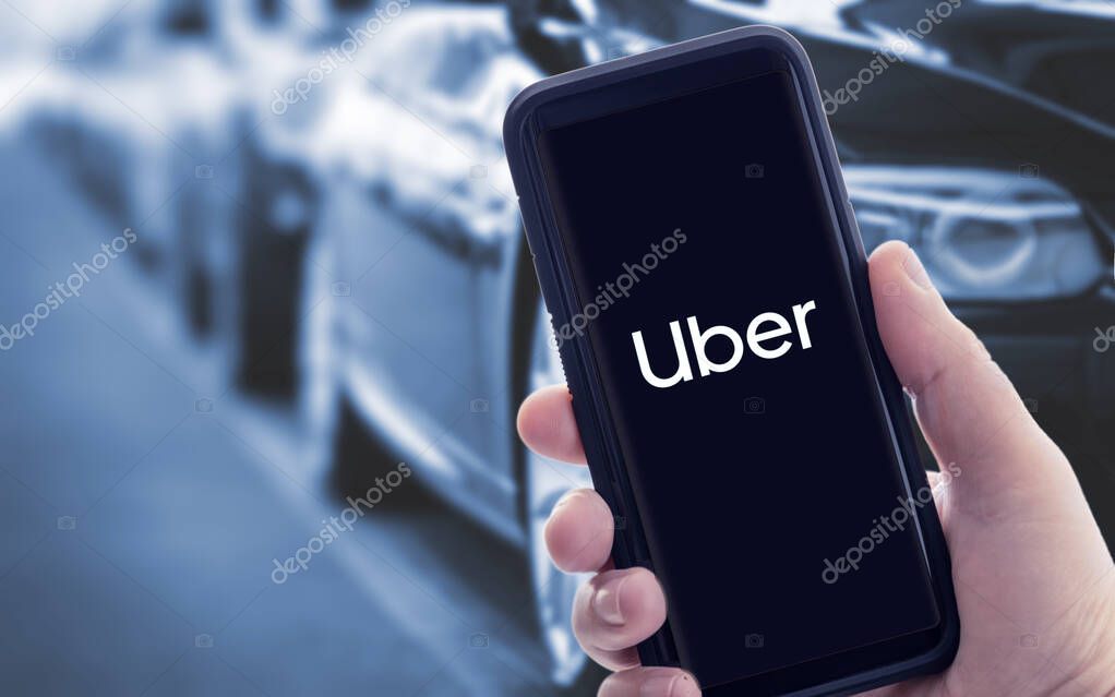 Galicia, Spain; january 09 2021: Hand holding a smart phone with Uber logo on screen and blurry cars on background