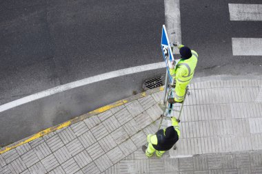İşçiler kaldırıma yeni bir yol tabelası asıyor. Kamu bakım kavramı