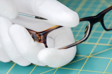 Optisyen eller bir aletle gözlük tamir ediyor. Kapat.