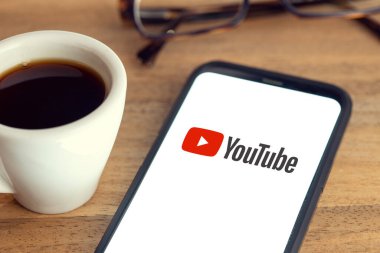 Galiçya, İspanya; 15 Şubat 2021: Akıllı telefon ekranında Youtube logosu, masasında gözlük ve ahşap masada bir fincan kahve