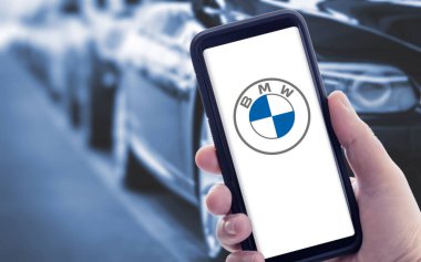 Galiçya, İspanya; Ocak 09 2021: Ekranda yeni BMW logosu ve arka planda bulanık arabalar olan akıllı bir telefon tutmak. Boşluğu kopyala