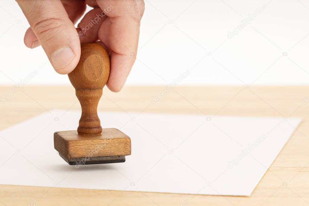 Hand holding a Rubber stamp and blank paper on wooden table. White background. Copy space