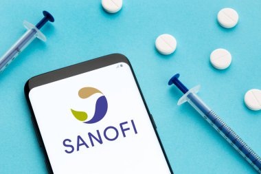 Galiçya, İspanya; 8 Haziran 2020: Ekranda Sanofi logosu, mavi arka planda haplar ve şırınga gösteren akıllı telefon