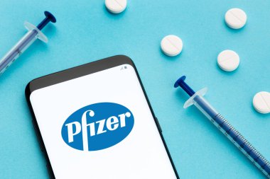 Galiçya, İspanya; 8 Haziran 2020: Ekranda Pfizer logosu, mavi arka planda haplar ve şırıngayı gösteren akıllı telefon