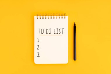 To do list in spiral notepad isolated on yellow background. Top view