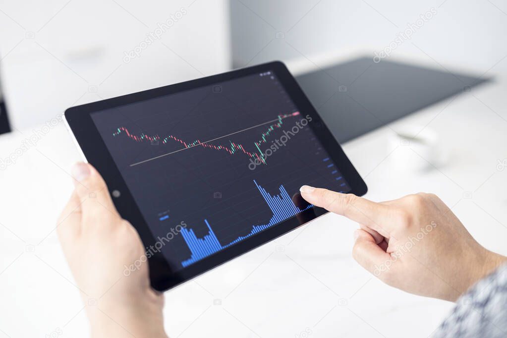 Woman holding a digital tablet with stock market chart in a modern kitchen. Trading at home concept
