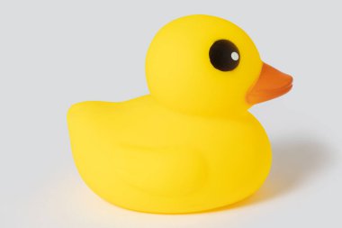 Sarı plastik ördek oyuncağı gri arka planda izole edilmiş, banyo zamanını sembolize ediyor ve oyun oynuyor