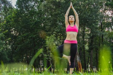 Hafif eşofmanlı Avrupalı bir kız yazın öğleden sonra parkta yoga yapıyor. Doğada jimnastik. Dışarıdaki zayıf kadın..