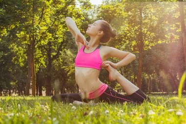 Hafif eşofmanlı Avrupalı bir kız yazın öğleden sonra parkta yoga yapıyor. Doğada jimnastik. Dışarıdaki zayıf kadın..
