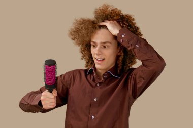 Bej arka planda kahverengi gömlekli uzun saçlı kıvırcık saçlı bir adam ahşap tarak kullanır. Bir kuaförde saç tıraşından önce duygular.