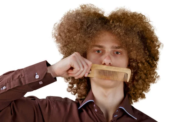 白地に茶色のシャツを着た長髪の巻き毛の男が木製の櫛を使用しています 美容室で散髪する前の感情 — ストック写真