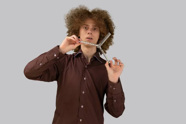灰色の背景に茶色のシャツを着た長髪の巻き毛の男は 金属櫛を使用しています 美容室で散髪する前の感情 — ストック写真