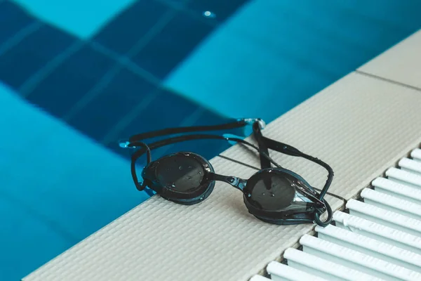swimming goggles are on the parapet near the swimming pool. indoor swimming sports equipment.