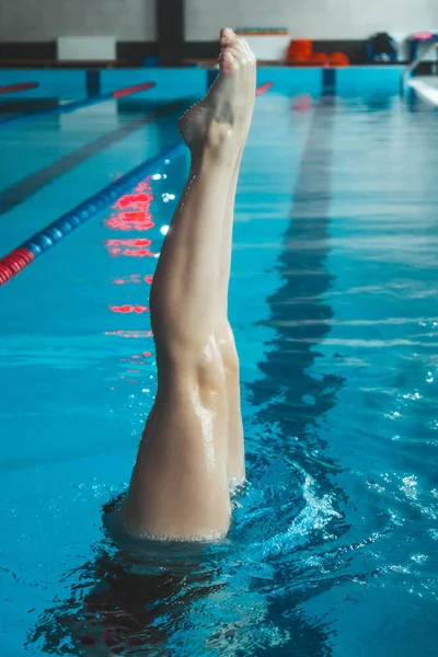 synchronized swimming athlete trains alone in the swimming pool. Training in the water upside down. Legs peek out of the water. sports figure from legs.