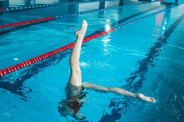 synchronized swimming athlete trains alone in the swimming pool. Training in the water upside down. Legs peek out of the water. sports figure from legs.