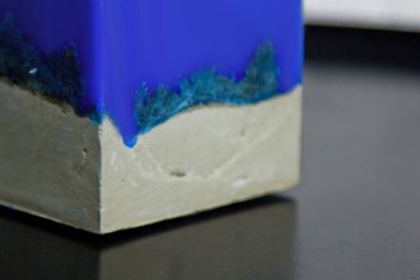 Beyaz bir duvarın arka planında beton olan ev yapımı mavi mum. El yapımı dekor yakın plan. Çatı katı biçiminde renkli mum detayları bir küp şeklinde.