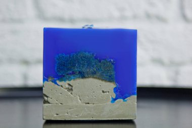 Beyaz bir duvarın arka planında beton olan ev yapımı mavi mum. El yapımı dekor yakın plan. Çatı katı biçiminde renkli mum detayları bir küp şeklinde.