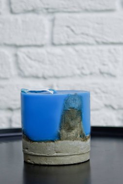 Beyaz bir duvarın arka planında beton olan ev yapımı sarı mum. El yapımı dekor yakın plan. Çatı katı biçiminde renkli mum ayrıntıları tüp şeklinde.