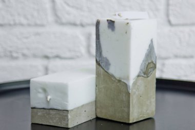 Beyaz bir duvarın arka planında beton olan ev yapımı beyaz mum. El yapımı dekor yakın plan. Çatı katı biçimindeki renkli mumların ayrıntıları küp şeklinde.