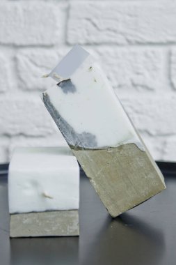 Beyaz bir duvarın arka planında beton olan ev yapımı beyaz mum. El yapımı dekor yakın plan. Çatı katı biçimindeki renkli mumların ayrıntıları küp şeklinde.