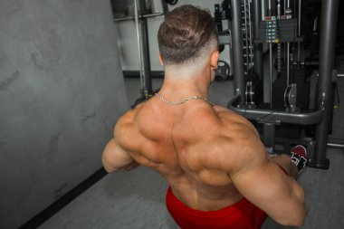 İri kaslı bir adam spor salonunda ağırlık kaldırmakla meşgul. Pompalı bir atlet spor için ağır sıklet simülatörleri kullanır. spor egzersizleri.