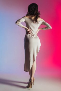 Rengarenk bir arka planda kısa bej elbisesi olan güzel bir esmer. Poz, mesaj, figür, zayıf kız. Reklam, kartpostal, dikey fotoğraf