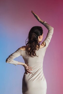 Rengarenk bir arka planda kısa bej elbisesi olan güzel bir esmer. Poz, mesaj, figür, zayıf kız. Reklam, kartpostal, dikey fotoğraf