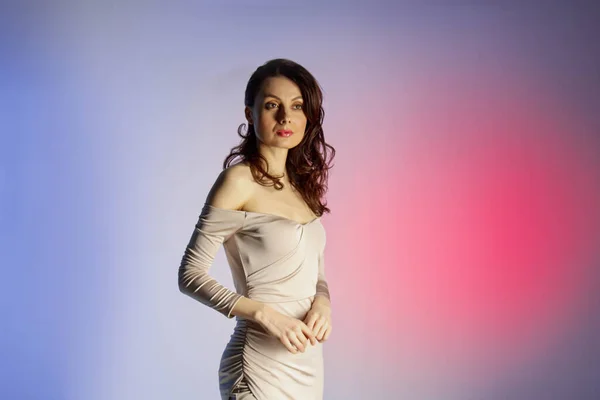 Colored background, neon lights, studio shot. Fashion portrait of a young elegant brunette woman in a nice dress