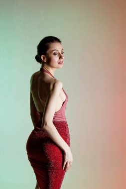 Renkli arka plan, neon ışıklar, stüdyo çekimi. Güzel elbiseli, zarif, esmer bir kadının moda portresi.