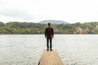 Göl kenarındaki ahşap iskelede yapayalnız duran bir adam.