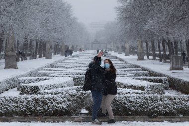 Madrid, İspanya - 07 Ocak 2021: Genç bir çift, Madrid 'deki Buen Retiro parkında kutup soğuğu dalgası nedeniyle cep telefonlarıyla selfie çekiyor..