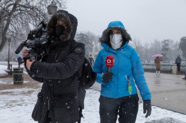 Madrid, İspanya - 07 Ocak 2021: Bir gazeteci ve bir Telemadrid kamera operatörü, Madrid 'deki Buen Retiro parkında çalışıyor, kar yağışlı bir günün ortasında,.