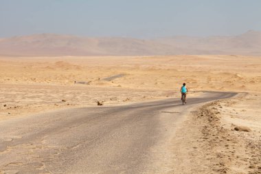 Çölün ortasındaki Ruta a Lagunillas boyunca bisiklet süren bir kadın, Paracas Ulusal Rezervi 'nde Playa Las Minas yakınlarında, Pisco, Ica Bölümü, Peru.