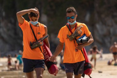 San Pedro de la Ribera, İspanya - 16 Ağustos 2020: Kamu Güvenlik Servisi 'nden birkaç cankurtaran yazın ortasında Asturias' ta bir plajda koruyucu yüz maskesi takarak yürüyor.