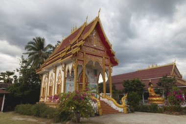 Cemaat ve büyüleyici Budist tapınağı Wat Phone Pang, gün batımında, Muang, Laos, Pakse 'den çok uzak olmayan Mekong nehrinin kıyısında, altın motifler ve Buda' nın kabartmaları ile süslenmiş..