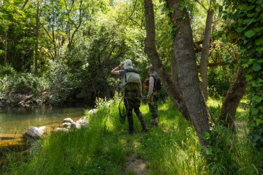 Segovia, İspanya - 2 Haziran 2021: İki balıkçı Senda de los Molinos üzerinden Segovia 'dan geçerken Eresma Nehri' nde iyi bir balıkçı noktası arıyorlar